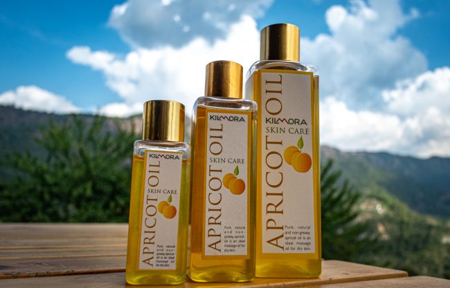 Three bottles of different sizes of Kilmora's cold pressed apricot oil in the foreground. With blue skies and some clouds showing at the back