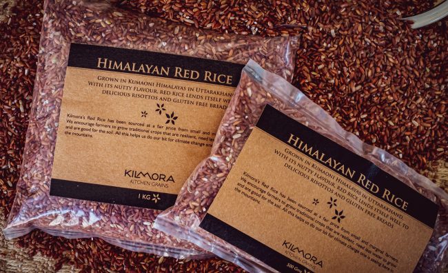 Two packets of Himalayan Red Rice of differing weights on a bed of loose red rice