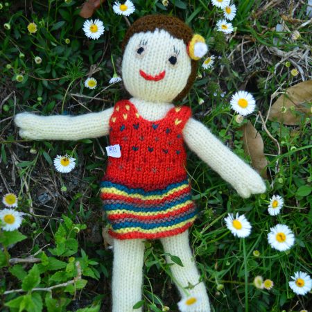 Knitted soft toy of a small girl in a red from lying o a bed of flowers