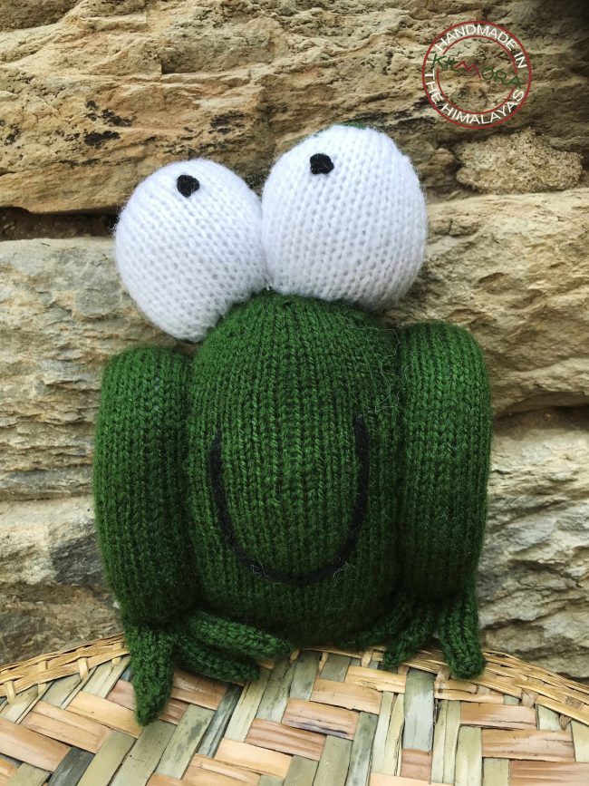 Knitted soft toy in the shape of a frog with bulging eyes and a huge smile