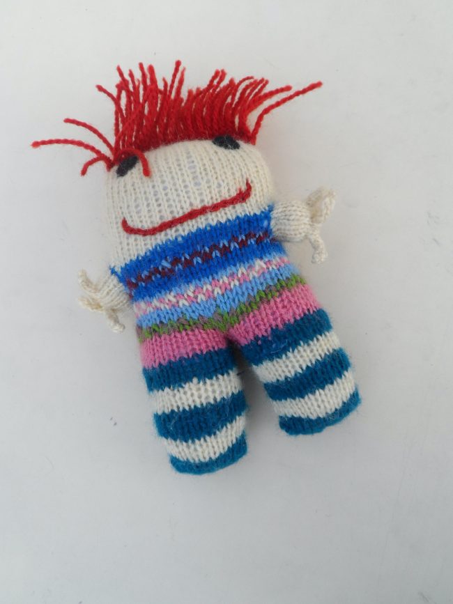 Knitted soft toy of a funky looking person with wild orange hair and a mischevious smile