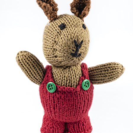 Hand-knit cotton toy of a rabbit wearing a red jumper with green buttons