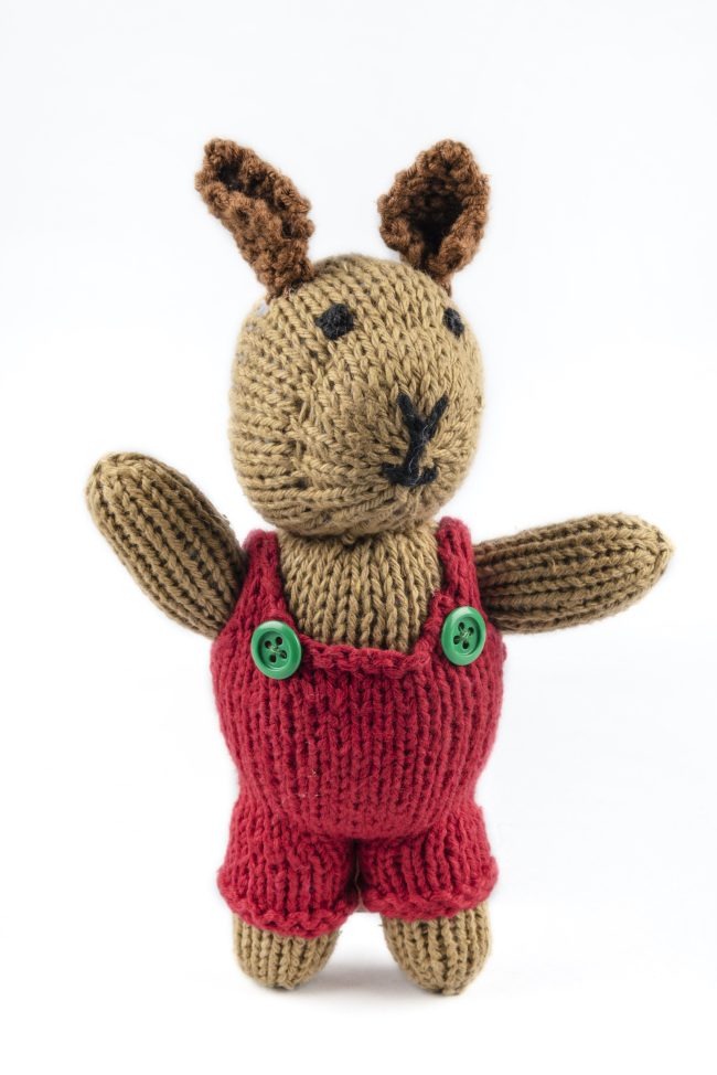 Hand-knit cotton toy of a rabbit wearing a red jumper with green buttons