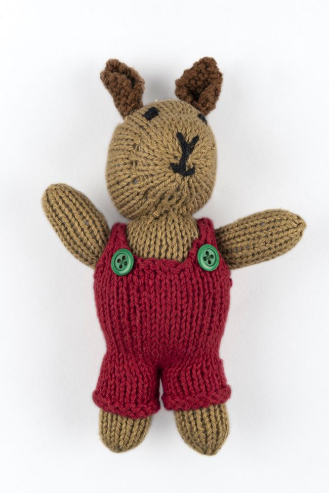 Hand-knit cotton toy of a rabbit wearing a red jumper with green buttons