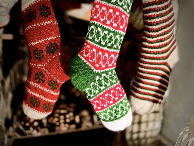 Hand knit Christmas stocking in 3 different patterns hanging in front of a stone fireplace