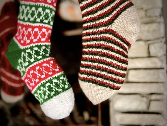 Hand knit Christmas stocking in 2 different patterns hanging in front of a stone fireplace