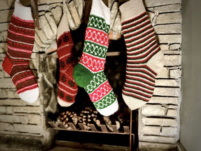 Hand knit Christmas stocking in 4 different patterns hanging in front of a stone fireplace