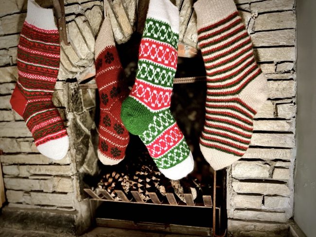 Hand knit Christmas stocking in 4 different patterns hanging in front of a stone fireplace