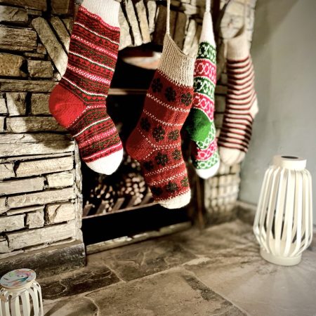 Hand knit Christmas stocking in 4 different patterns hanging in front of a stone fireplace