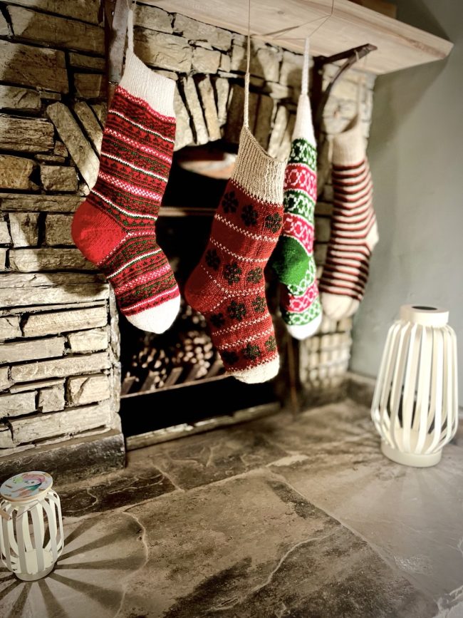 Hand knit Christmas stocking in 4 different patterns hanging in front of a stone fireplace