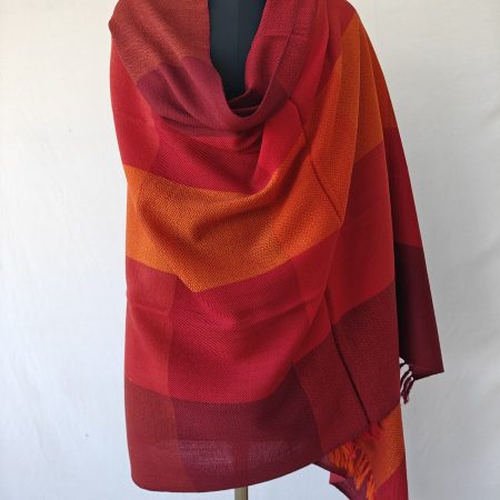 Merino wool shawl draped on a mannequin in bold checks in shades of scarlet, wine and pepper