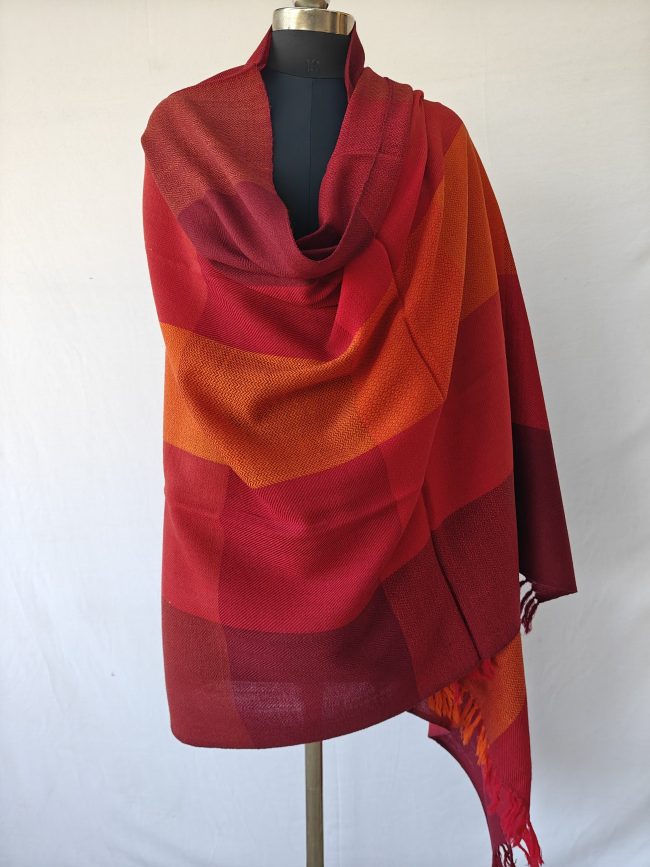 Merino wool shawl draped on a mannequin in bold checks in shades of scarlet, wine and pepper