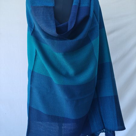 Merino wool shawl draped on a mannequin. In bold blue checks in shades of aquamarine, royal blue and Egyptian blue