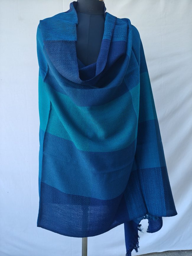 Merino wool shawl draped on a mannequin. In bold blue checks in shades of aquamarine, royal blue and Egyptian blue